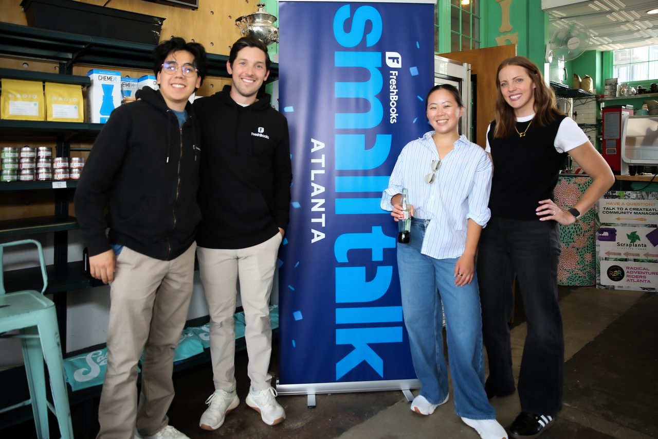 FreshBooks team posing beside a Small Talk Atlanta banner