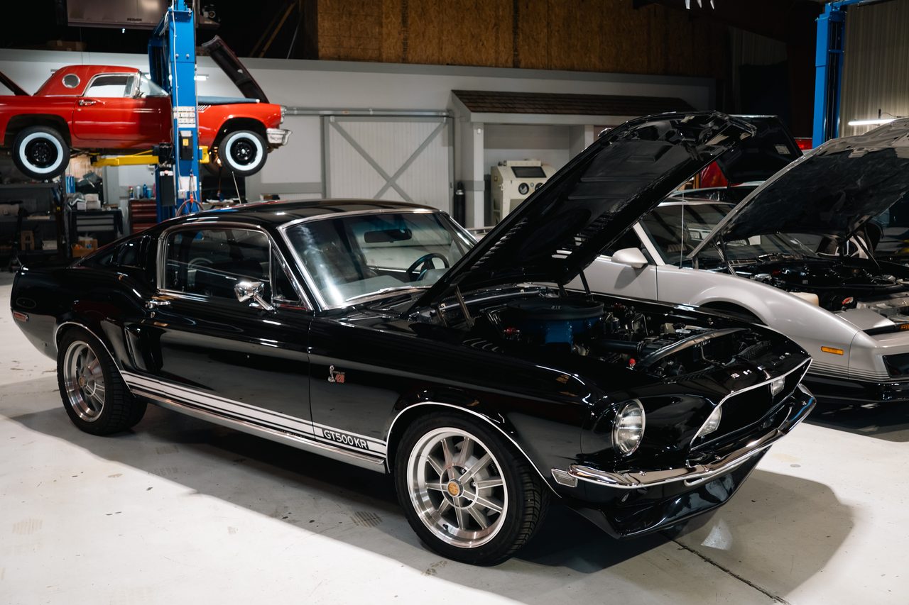Black 1968 Shelby Mustang with its hood open in a collector warehouse