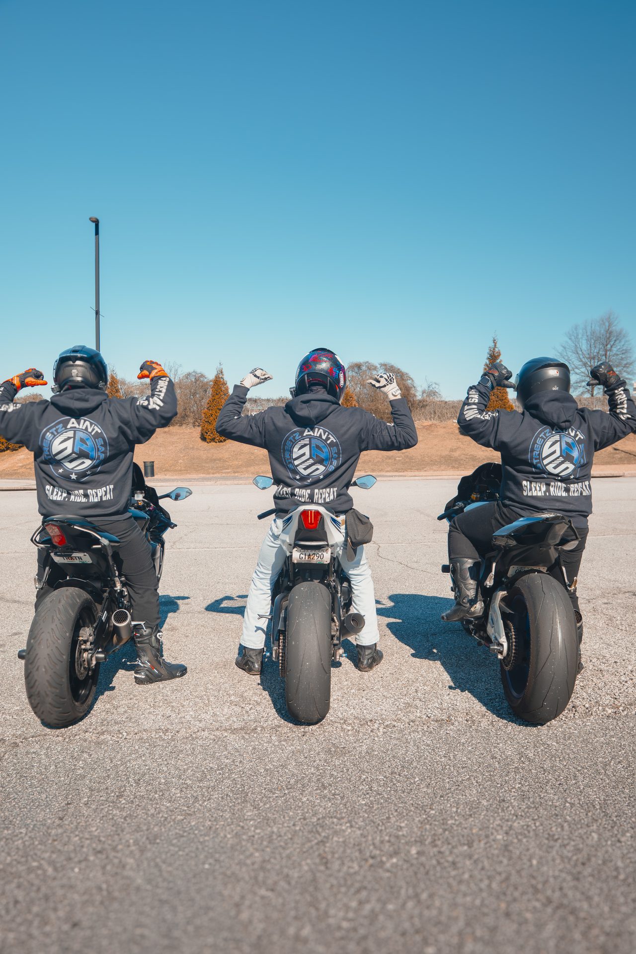 Three riders with their bikes lined up under a blue sky