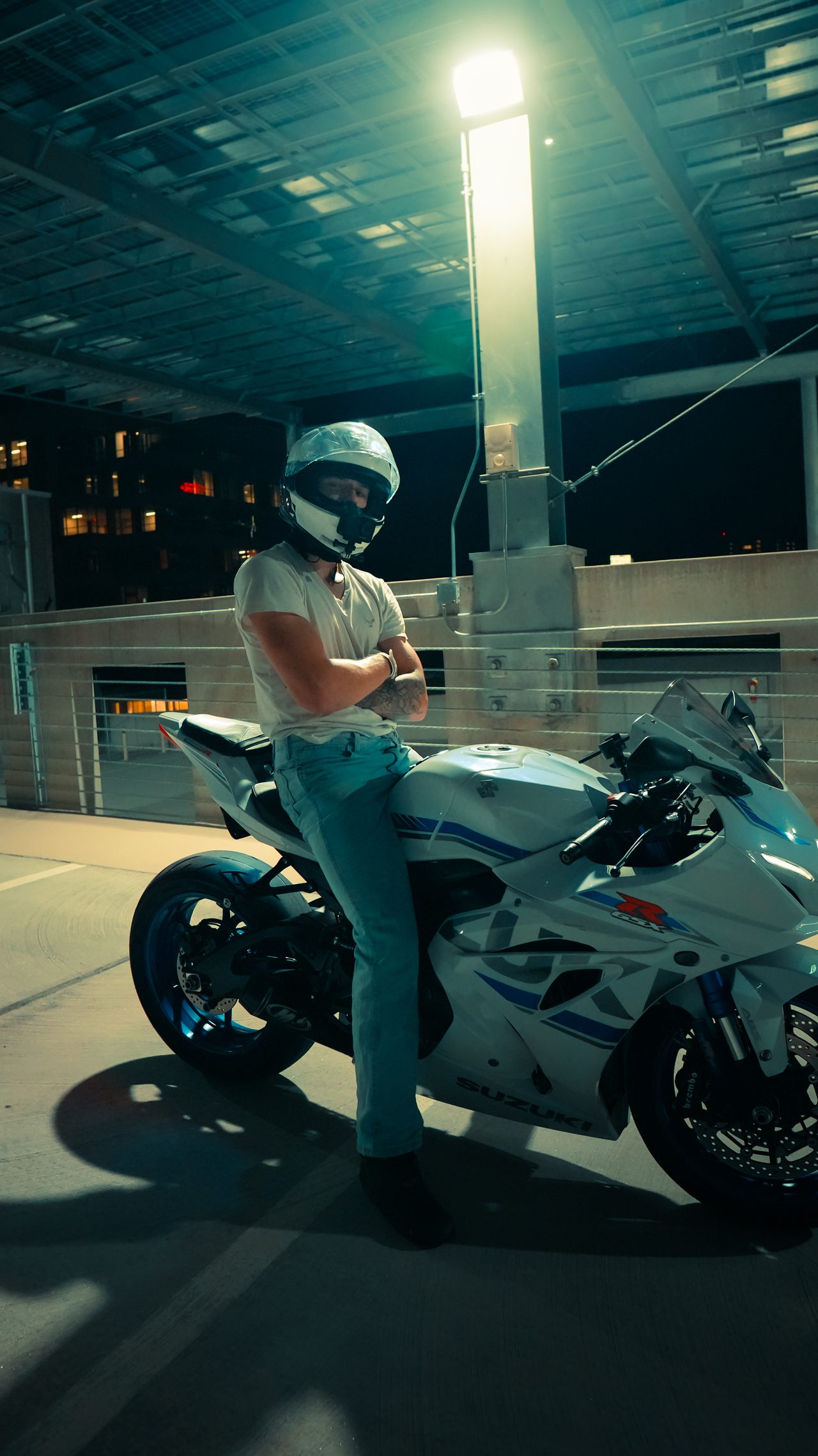 Rider beside a motorcycle under a single overhead light at night