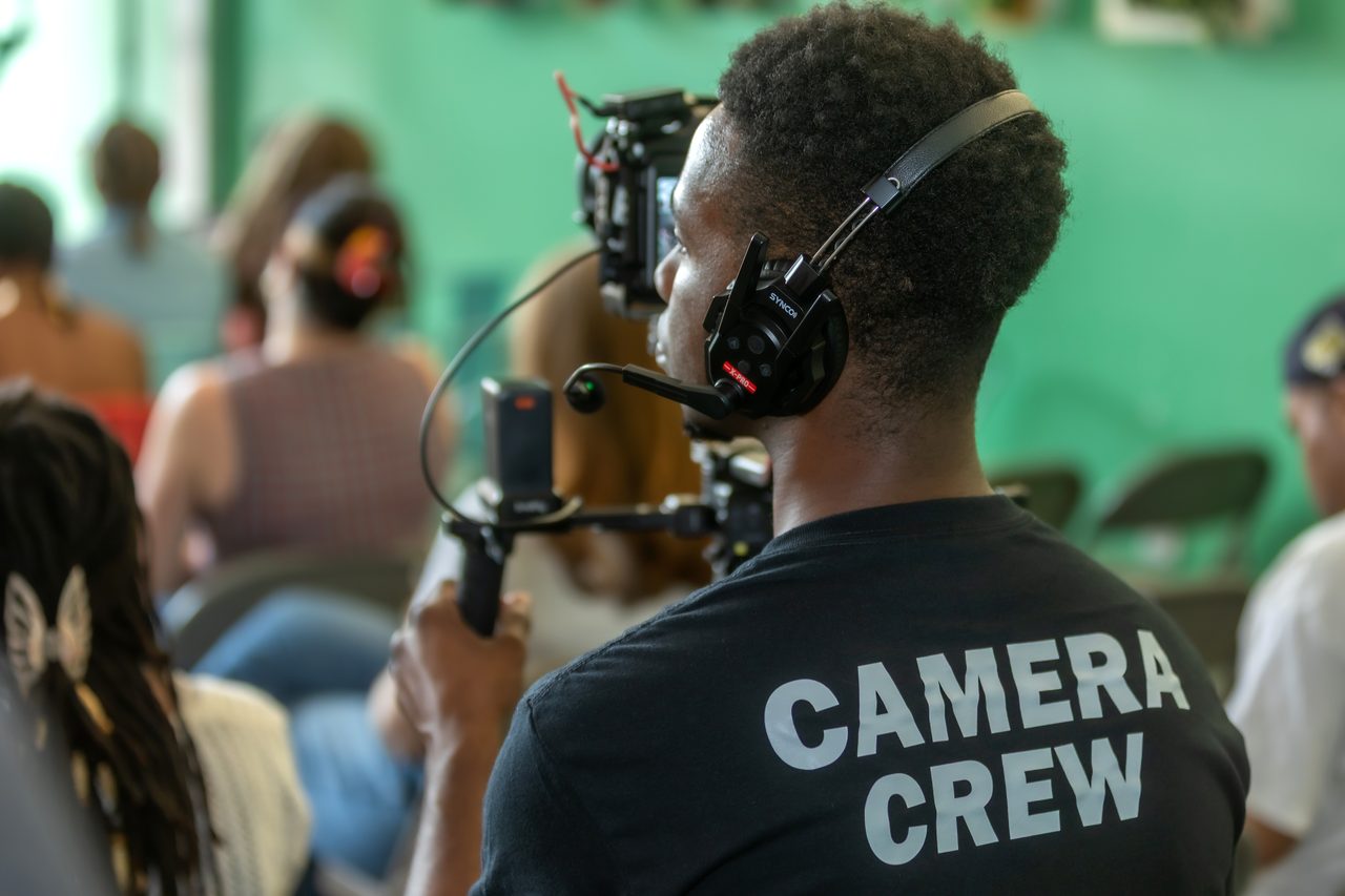 Camera operator in a Camera Crew shirt filming a seated audience